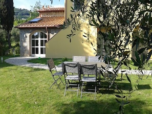 A stone building with a tiled roof, a glass door, and a small patio with a table and chairs. - Apartment in Tuscany With Scenic Pool Views (Capannori)