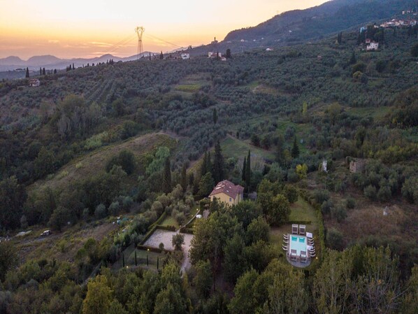Una propiedad en una ladera con piscina, una casita y vegetación circundante.