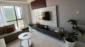 Una sala moderna con un sofá, una mesa de centro, un televisor montado en una pared de mármol y un ventanal con vistas a la ciudad.
