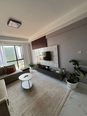 A modern living room with a sofa, a coffee table, a TV mounted on a marble wall, and a large window with a city view. - Fluted Nest on 16 Floor with views 
Kilimani (Nairobi)