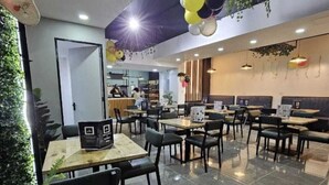 Un restaurante con cabinas y mesas, techo con plantas colgantes, y una fuente de luz brillante.