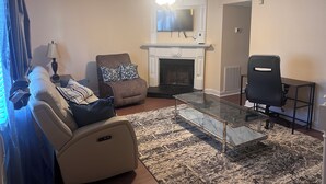 A living room with a sofa, armchair, fireplace, television, and a glass coffee table. - 2BR Townhome Near Hospitals Free Parking Wi-Fi  (Norcross)