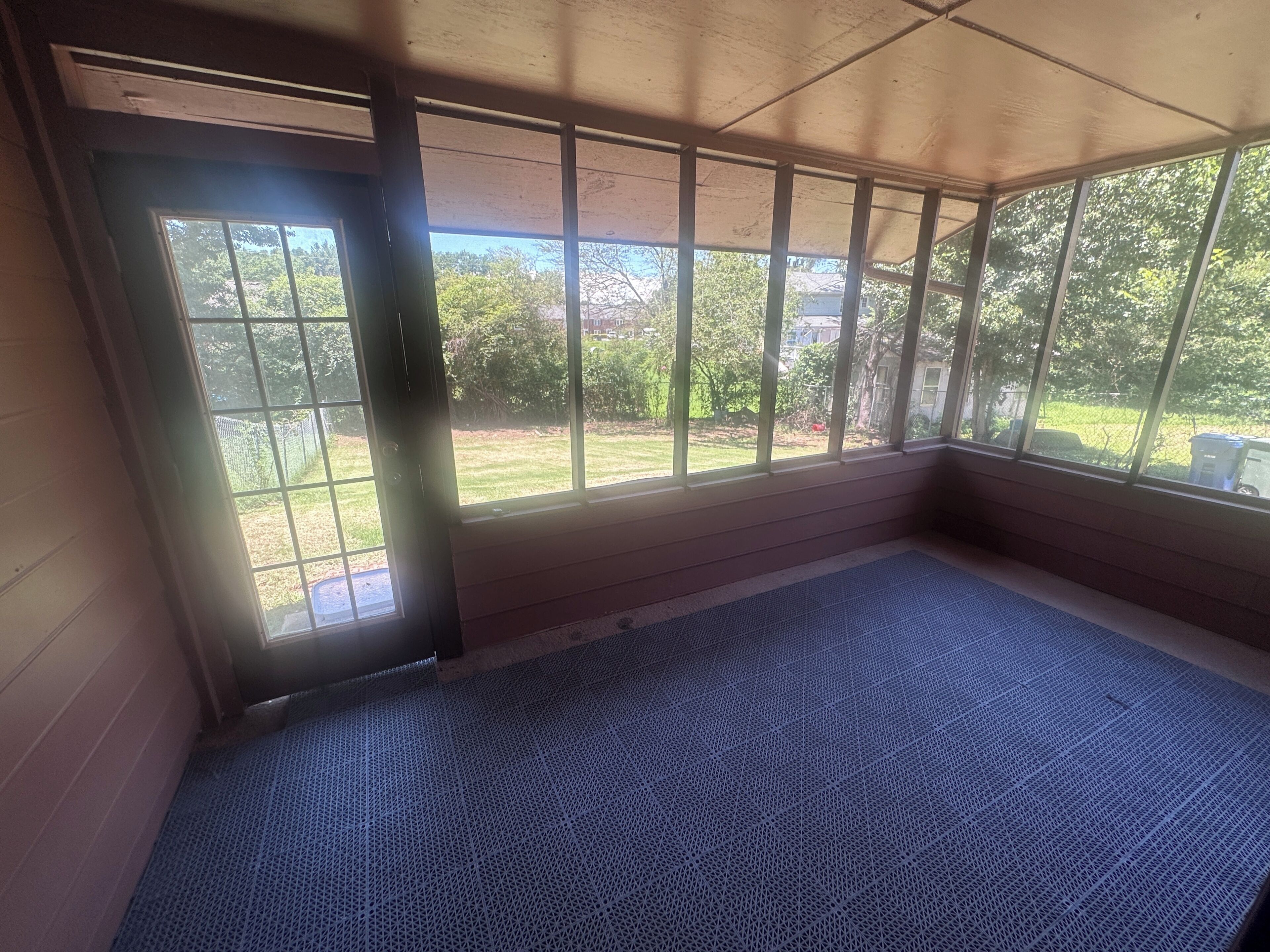 Quarto com uma janela grande, um tapete azul e uma porta.