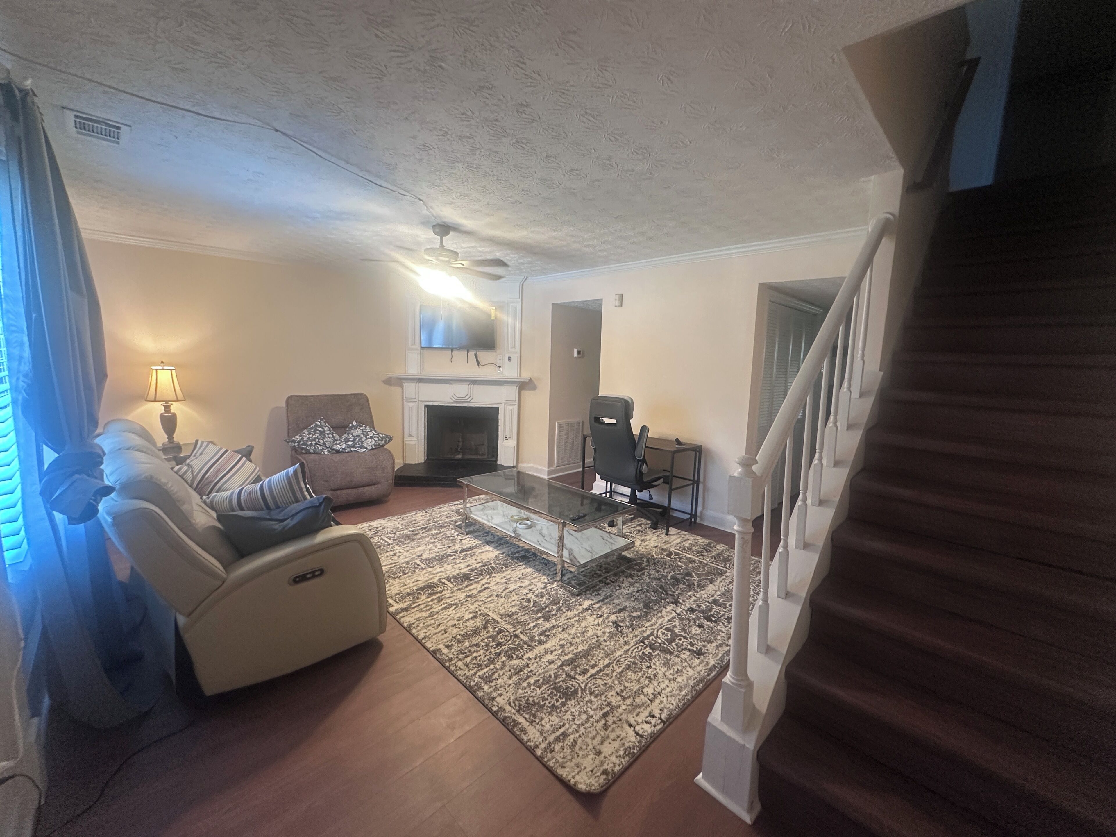 Una sala de estar con sofá, sillón, mesa de centro, chimenea y una escalera.