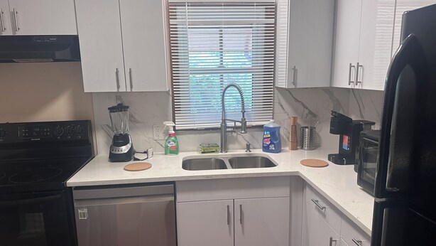 A kitchen with white cabinets, a built-in oven, a sink, a coffee maker, and a window with blinds. - 2BR Townhome Near Hospitals Free Parking Wi-Fi  (Norcross)