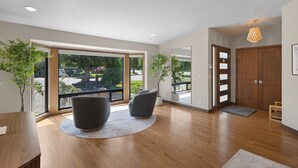 Habitación amplia con un gran ventanal corredero que da a un balcón, dos sillones oscuros, una mesa de madera y una planta en maceta.