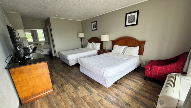 A hotel room with two beds, a wooden dresser, a desk with a computer, and a red chair. - Bayou Inn (Jennings)