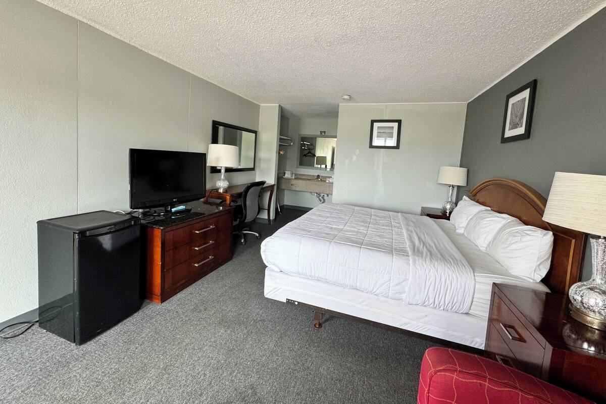 A hotel room with a bed, a desk, a television, a dresser, and a bathroom.