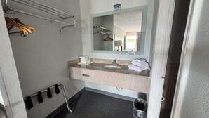 A hotel bathroom with a sink, mirror, towel rack, and a trash bin. - Bayou Inn (Jennings)