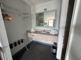Un baño de hotel con lavamanos, espejo, toallero y un cesto de basura.