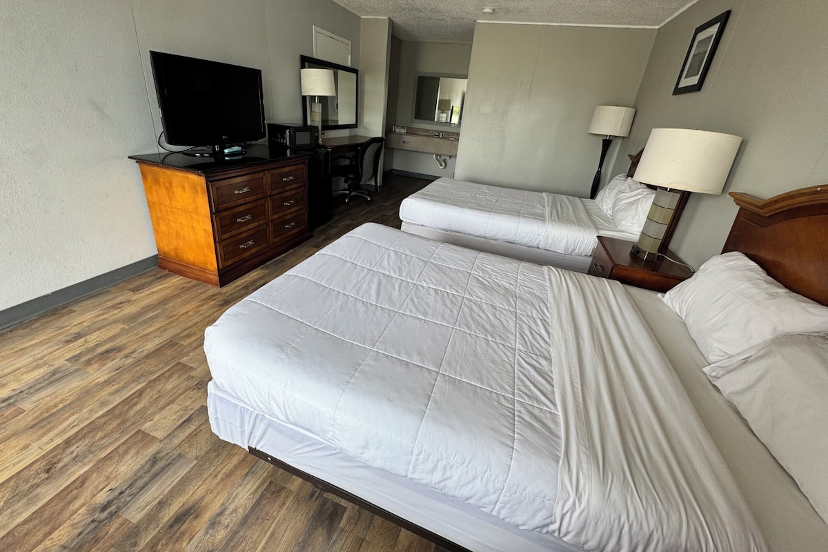 A hotel room with two beds, a desk, a television, and a mirror.