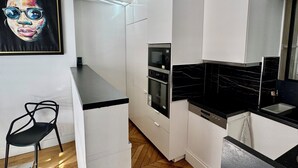 A modern kitchen with white cabinetry, a black countertop, a microwave, and a wooden herringbone floor. - Luxury Apartment Paris Trocadero - 2 bedrooms 80m2 (Paris)