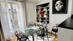 A modern dining area with a glass table, black chairs, a striped rug, a bookshelf, and a painting on the wall. - Luxury Apartment Paris Trocadero - 2 bedrooms 80m2 (Paris)