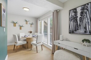 Een moderne kamer met een eettafel, stoelen, een bureau en een groot schilderij in een lijst aan de muur.