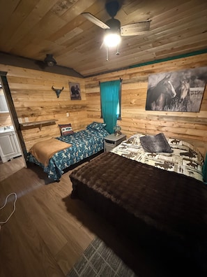 A rustic wooden room with a bed, a bench, a ceiling fan, and a wall-mounted picture.