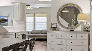 A modern kitchen with white cabinetry, a dining area with a table and chairs, a grey sofa, a large decorative mirror, and a Wi-Fi sign. - Cozy Downtown Home W/ Beautiful City Views! (Houston)