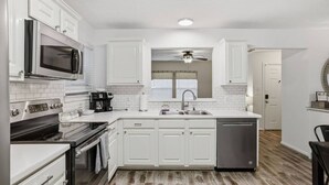 A modern kitchen with white cabinetry, a microwave, an oven, a dishwasher, and a ceiling fan. - Cozy Downtown Home W/ Beautiful City Views! (Houston)