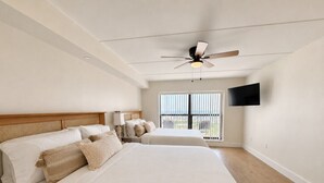 A hotel room with two beds, a ceiling fan, a TV mounted on the wall, and a balcony with a view. - Saida IV Condos - S4904 (South Padre Island)