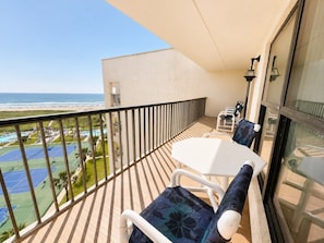 A balcony with a white table and chairs, overlooking a beach and tennis courts. - Saida IV Condos - S4904 (South Padre Island)
