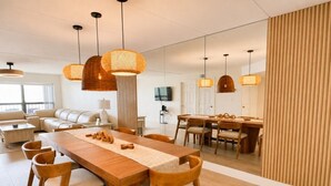 A modern dining area with a wooden table and chairs, pendant lights, and a television in the background. - Saida IV Condos - S4904 (South Padre Island)
