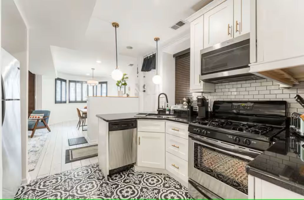 A modern kitchen with white cabinets, a black stove, and pendant lighting.