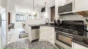 Une cuisine moderne avec des meubles blancs, une cuisinière noire et des luminaires suspendus.