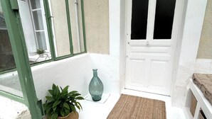 A room with a white door, a window with green frames, a woven mat, and a potted plant.