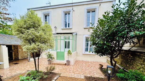 A building with a stone-paved courtyard, a green door, and potted plants.