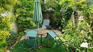A patio area with a table and chairs, surrounded by lush greenery and a stone wall.