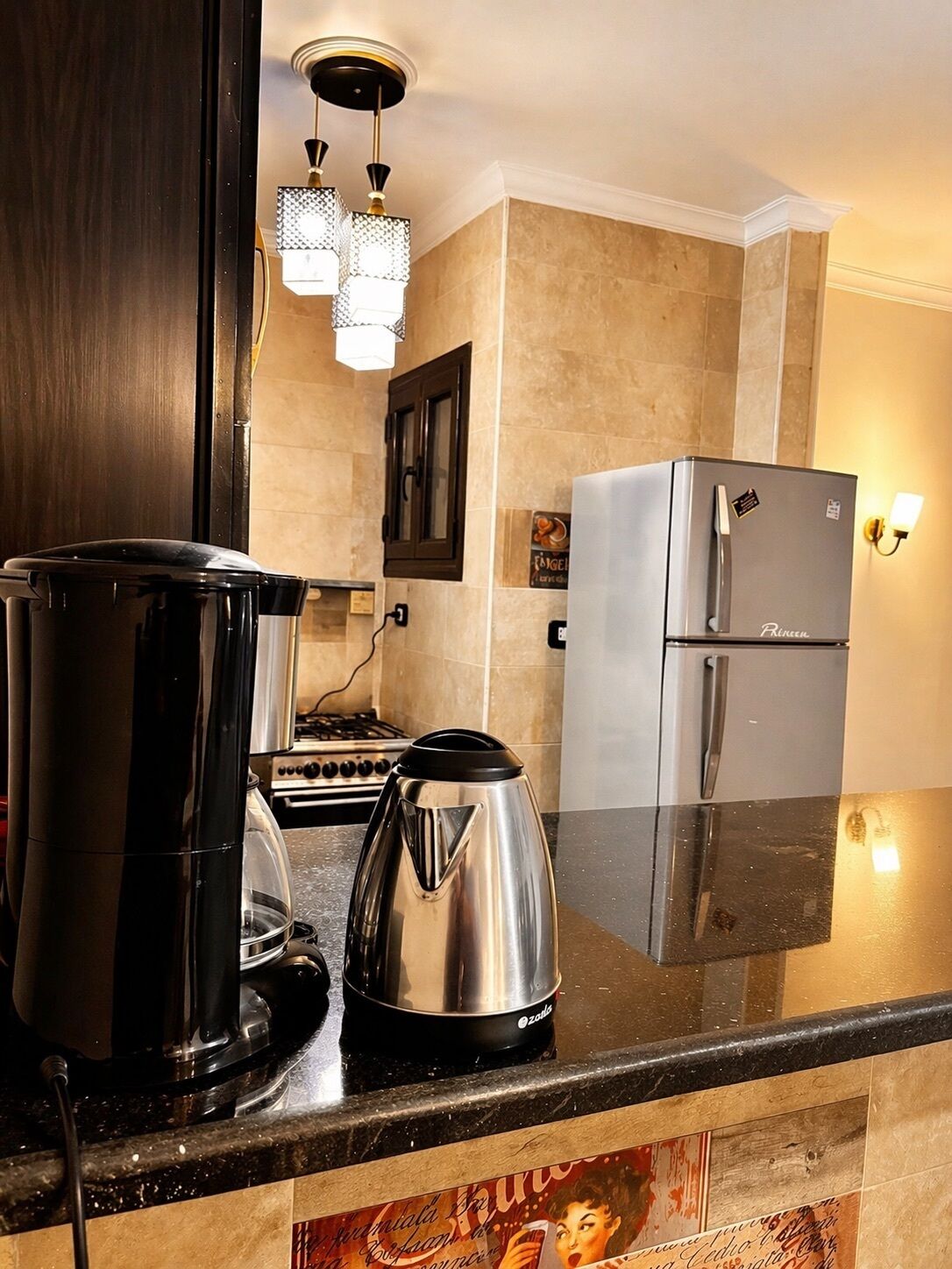 Een keuken met een fornuis, waterkoker, koelkast en koffiezetapparaat.