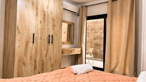 Ein Schlafzimmer mit Bett, einem Holzschrank, einem Spiegel, einem Fenster mit Vorhängen und Blick ins Freie.