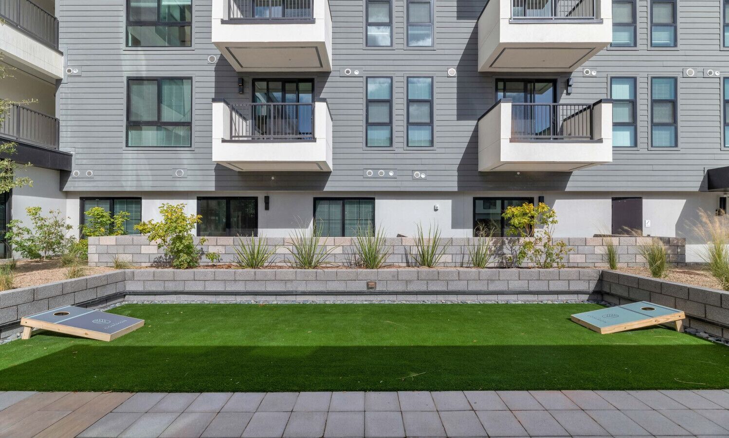 Un immeuble d’appartements moderne, doté d’un toit plat, de balcons et d’une pelouse bien entretenue agrémentée de deux jardinières en bois.