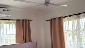 Ein modernes Schlafzimmer mit Bett, Vorhängen, Deckenventilator und Fenster mit Blick.