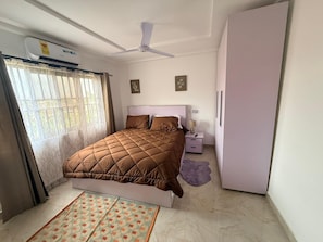 Un dormitorio con cama, mesita de noche, ventilador de techo, armario y ventana con cortinas.
