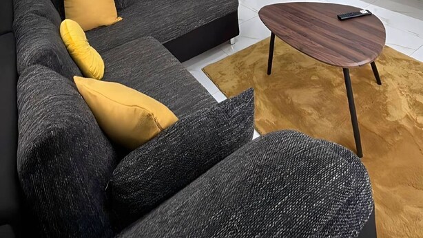 Ein modernes Wohnzimmer mit einer Eckcouch, einem Couchtisch, einem Essbereich mit Stühlen und einem an der Wand montierten Fernseher.