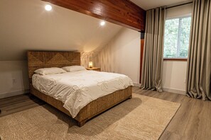 Een slaapkamer met een groot bed, een nachtkastje, een raam met gordijnen en houten balken in het plafond.