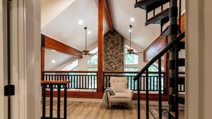 Amplia habitación con techo alto, vigas de madera, pared de piedra, una silla y una escalera.