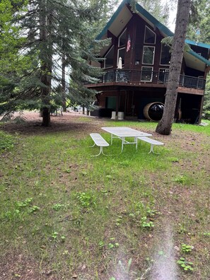 Een chalet met terras, een grote boom en een picknicktafel in de voortuin.