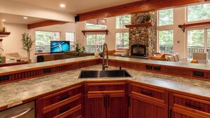 Una cocina con chimenea de piedra, armarios de madera, encimera de granito y televisor empotrado.