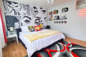 Une chambre à coucher comprenant un lit, une table de chevet, une lampe, un mur décoré d’illustrations représentant des yeux, et une étagère avec des disques.