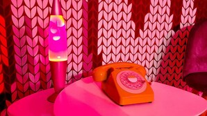 En retro orange telefon med drejeskive på et pink bord foran en væg med tapet.