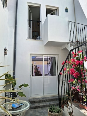 Ein weißes Gebäude mit Balkon, Treppe und Kübelpflanzen.