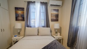 A hotel room with a bed, two bedside tables with lamps, a wall clock, and two paintings. - Cozy St. James Beach Villa – Steps from the Ocean. (Fitts Village)