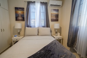 A hotel room with a bed, two bedside tables with lamps, a wall clock, and two paintings. - Cozy St. James Beach Villa – Steps from the Ocean. (Fitts Village)
