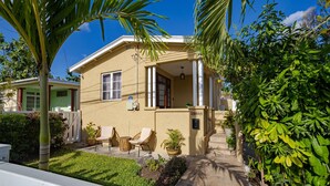 A two-story house with a covered patio, a small garden, and a palm tree. - Cozy St. James Beach Villa – Steps from the Ocean. (Fitts Village)