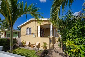 A two-story house with a covered patio, a small garden, and a palm tree. - Cozy St. James Beach Villa – Steps from the Ocean. (Fitts Village)