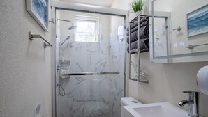 A bathroom with a glass-enclosed shower, a toilet, a sink, and a towel rack with towels. - Cozy St. James Beach Villa – Steps from the Ocean. (Fitts Village)