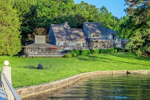 Ein großzügiges Haus mit einer Terrasse, umgeben von üppiger Vegetation und einem Teich.
