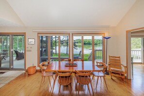 A dining area with a wooden table and chairs, large windows with a view of a lake, and a sliding glass door leading to an outdoor deck. - Refined Lakefront Home on Fort Loudon Lake - Dock + Sunset Views - Knoxville (Knoxville)