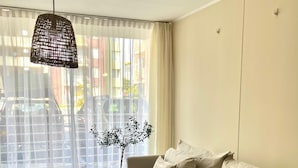 Een woonkamer met een bank, een tafel, een hanglamp, een potplant en uitzicht door een raam.